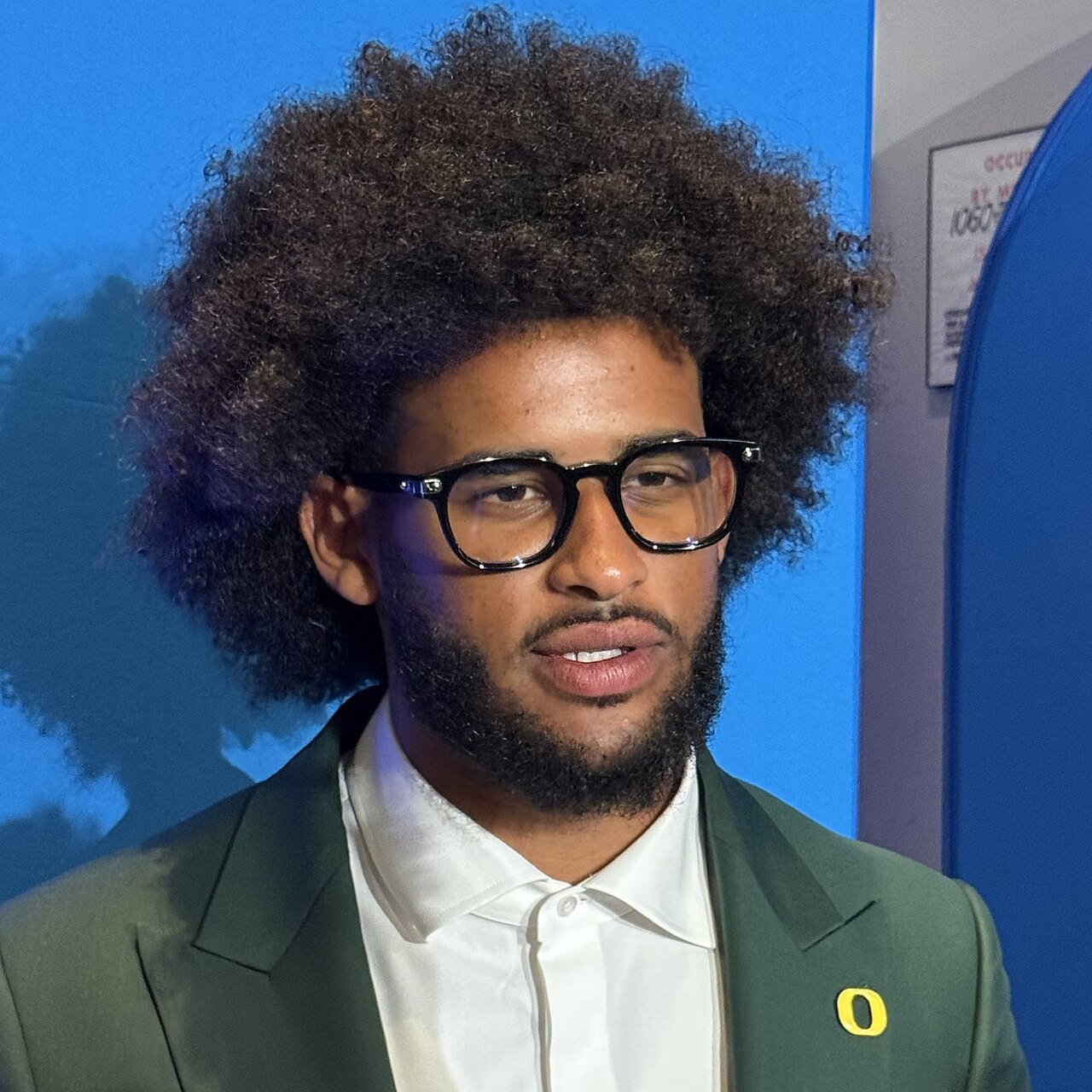Oregon quarterback Dante Moore wearing glasses and a green suit at Big Ten Football Media Days.