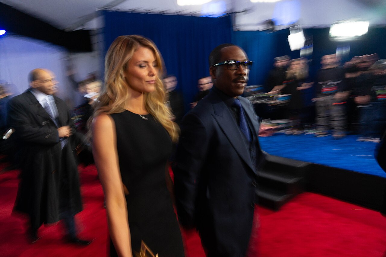 Eddie Murphy wearing dark glasses and a navy suit while walking the Saturday Night Live 40th anniversary red carpet in 2015.