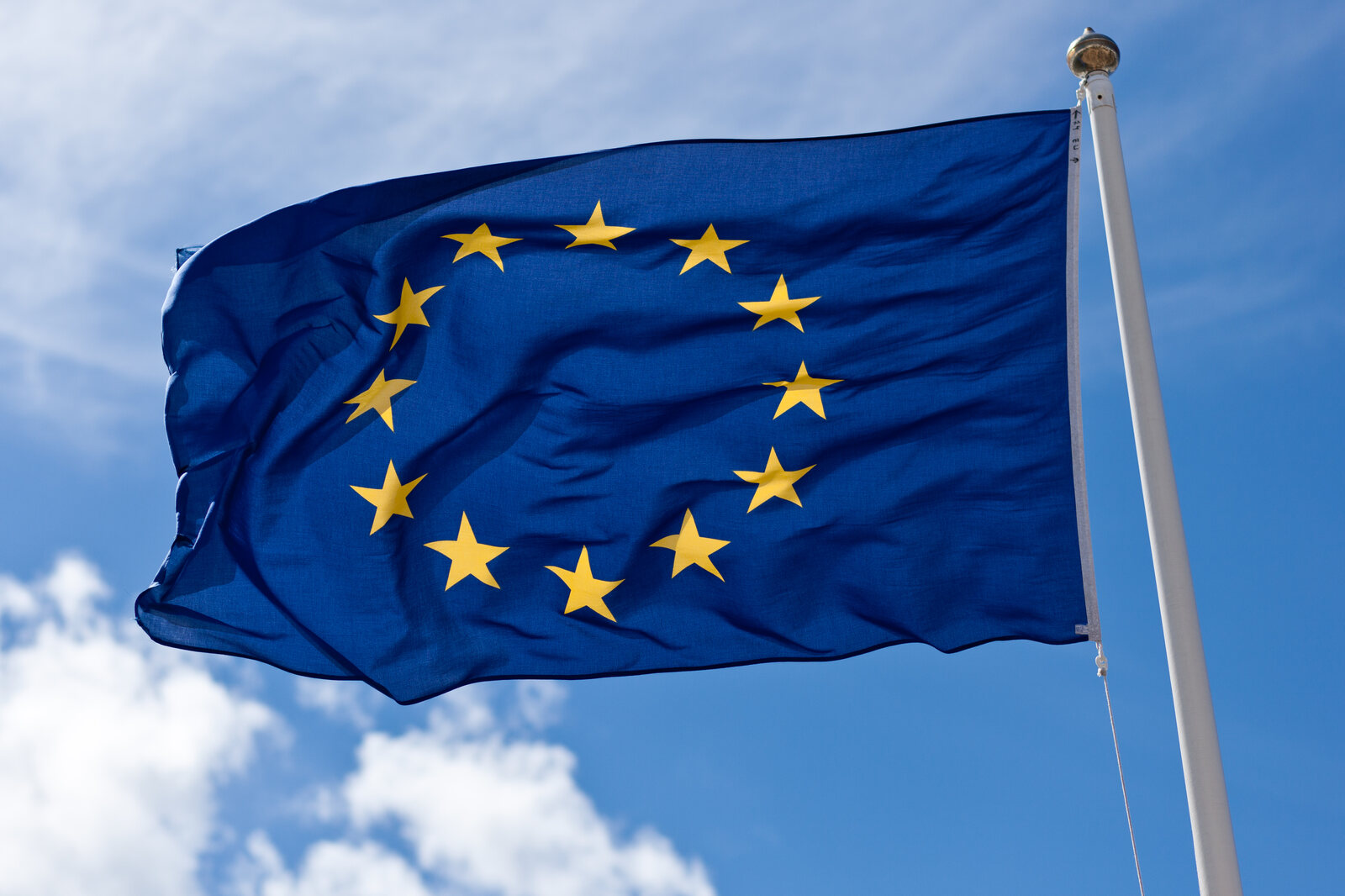 The blue European Union flag with yellow stars flying against a cloudy sky.