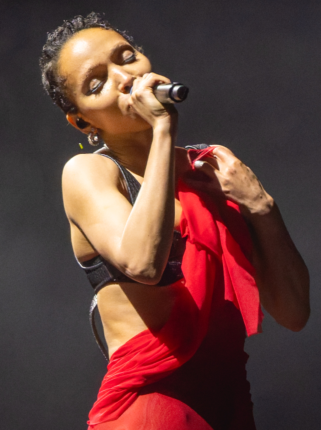 FKA twigs sings into a microphone while wearing a red-and-black stage outfit