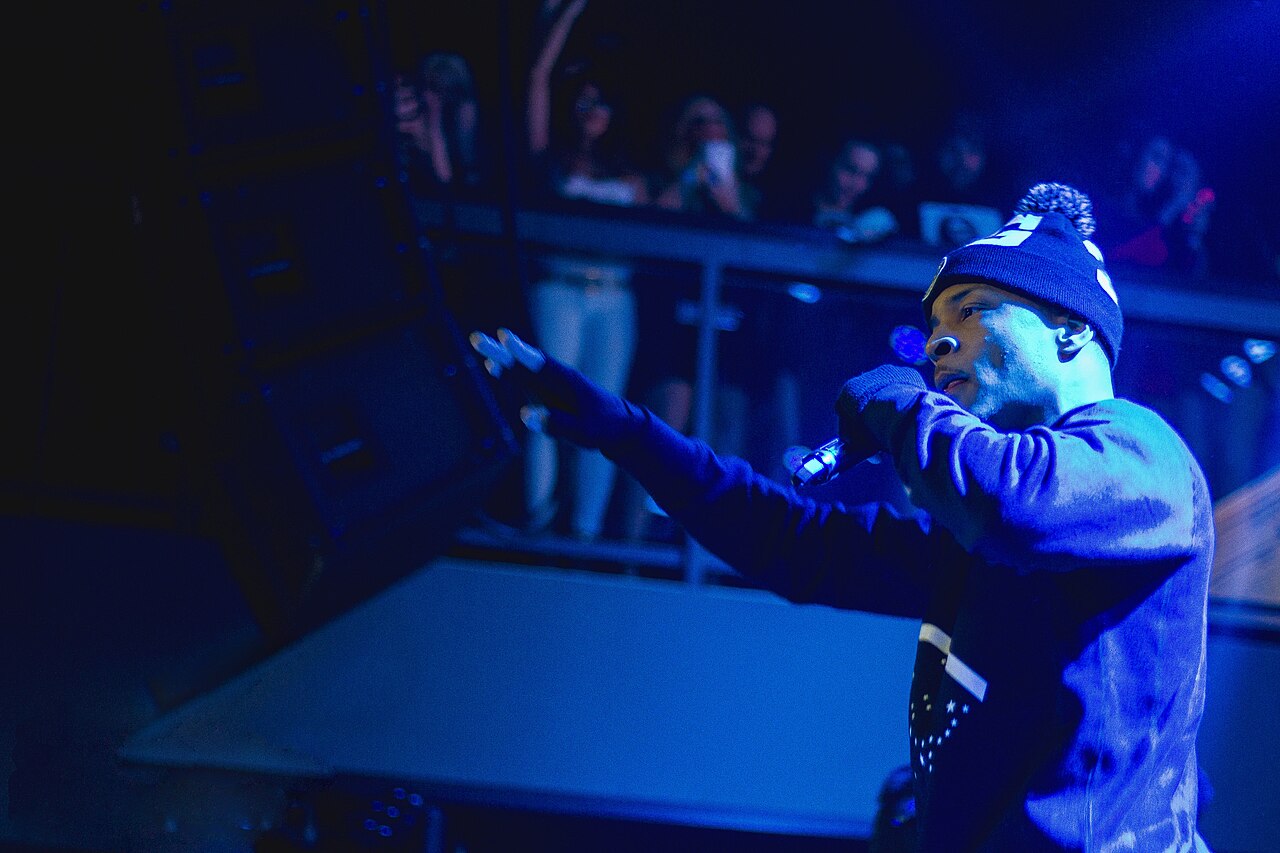 T.I. performing with a handheld microphone under blue concert lighting on his 2014 Paperwork tour.