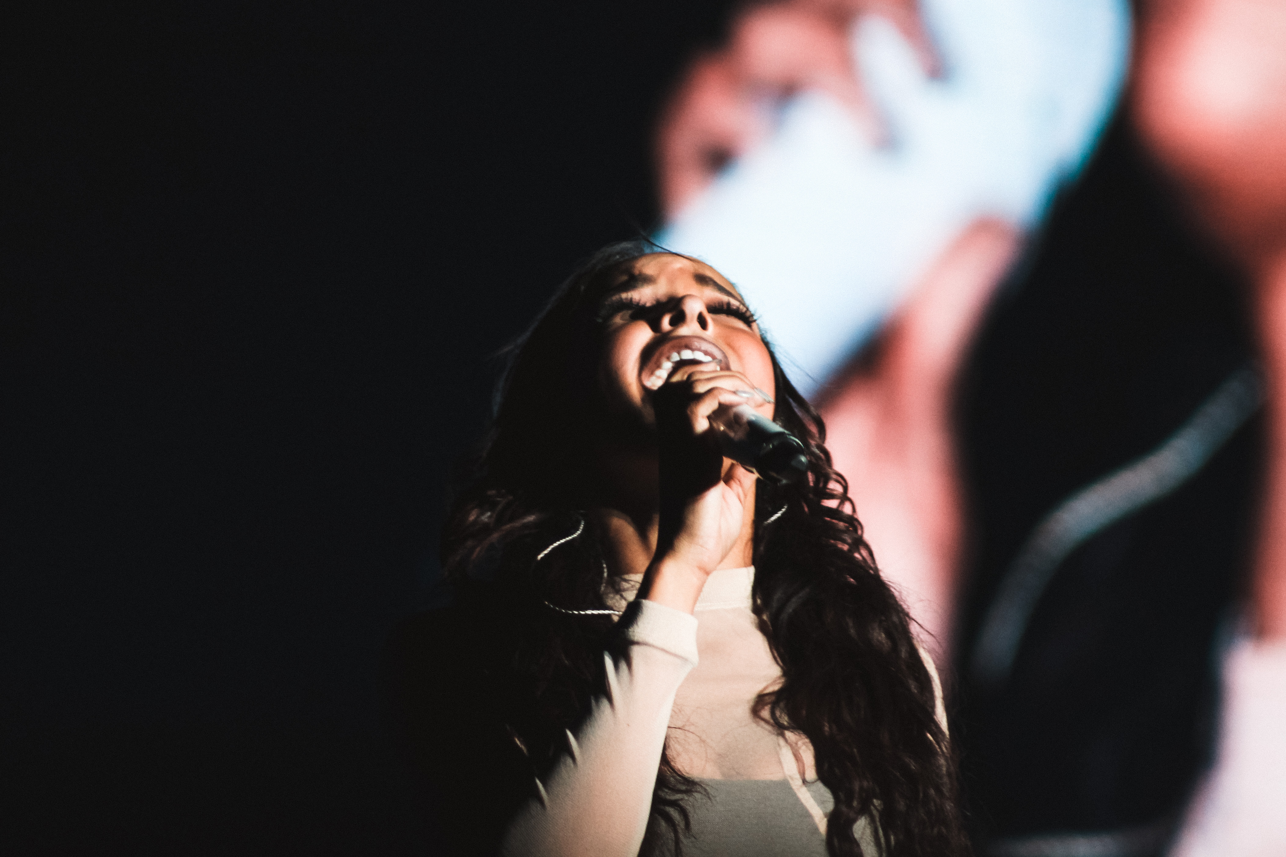 Tinashe singing into a handheld microphone onstage in an archival 2015 concert photograph.