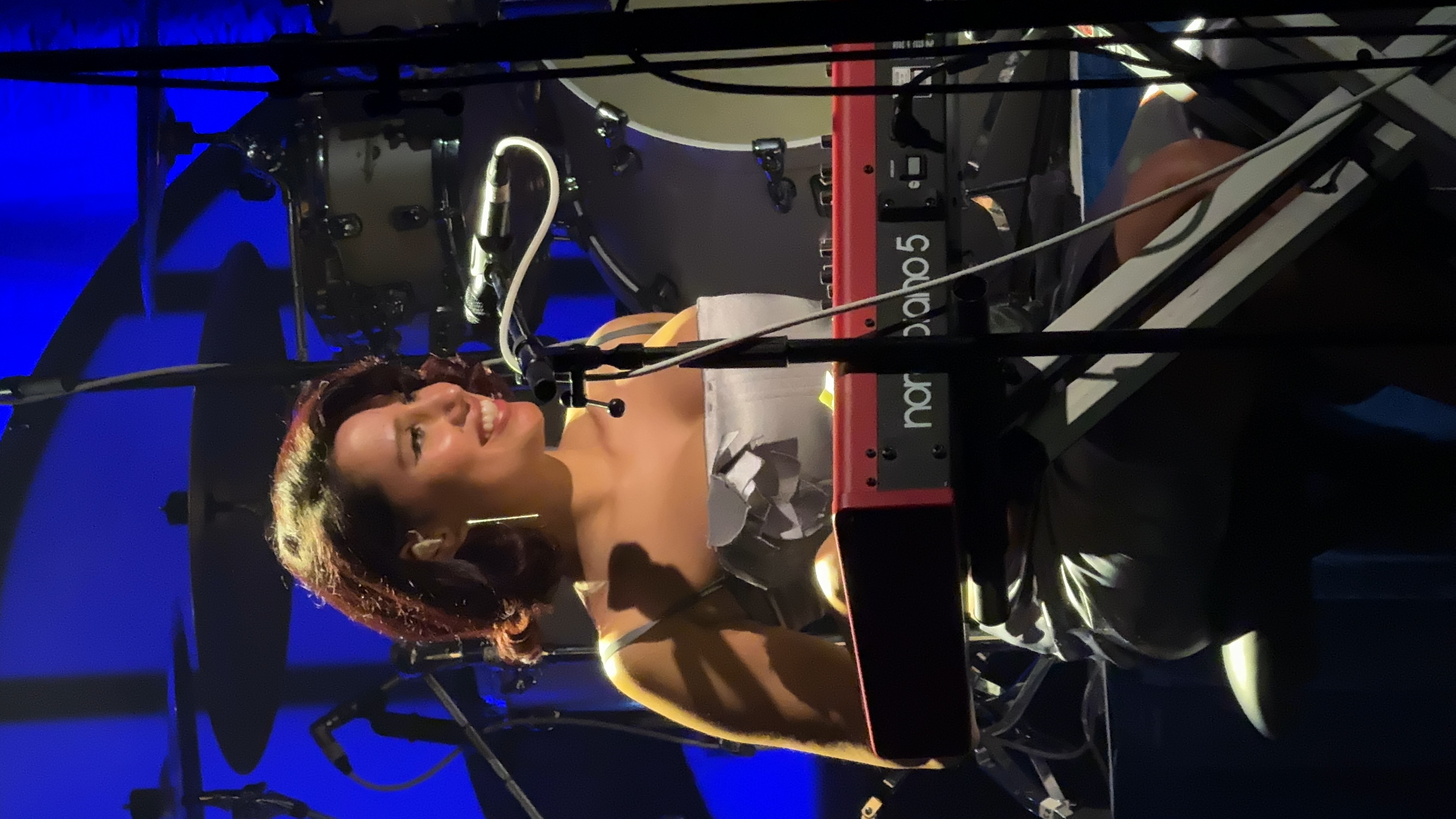 RAYE smiling at a microphone behind a keyboard during a 2023 performance