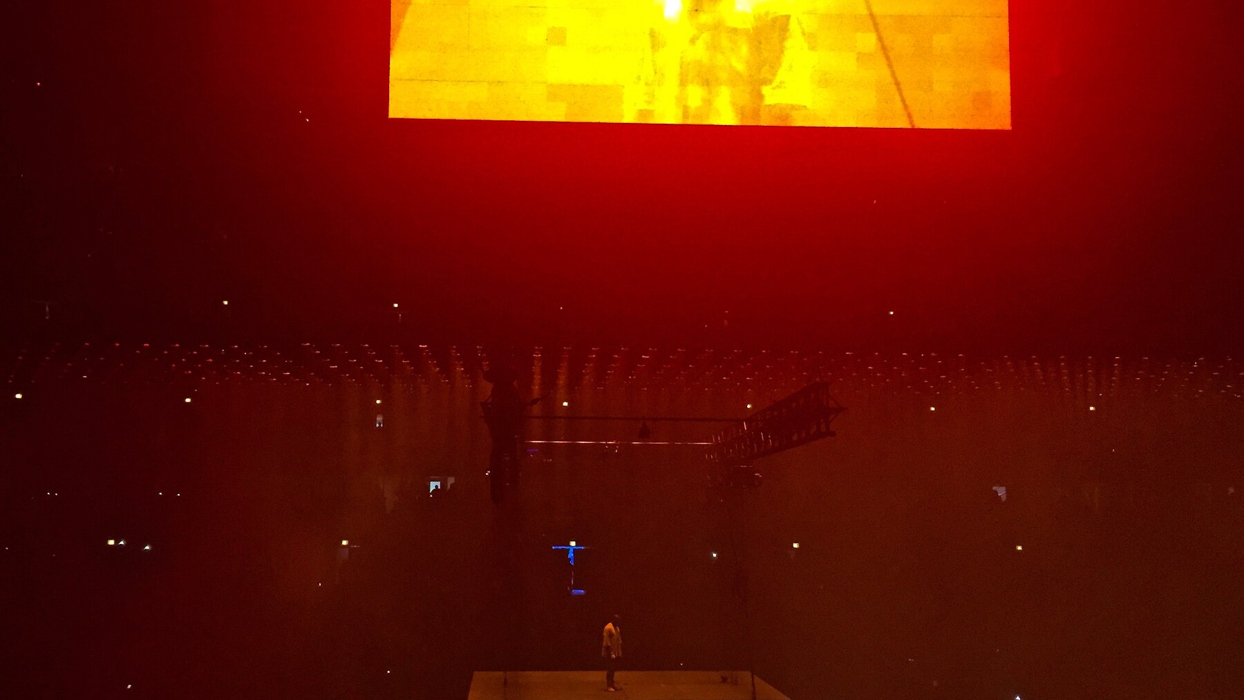 Ye performing on a suspended stage above a concert crowd under deep red lighting in Chicago.